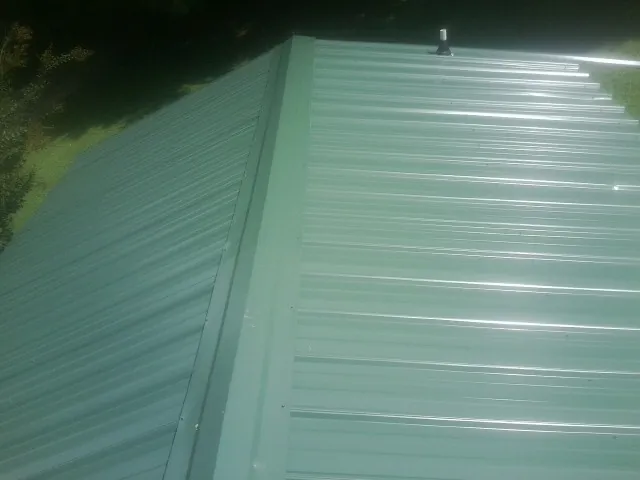 New green metal panels meeting at the ridge of a roof — Flat Roof Repair work by our crew in Pembroke